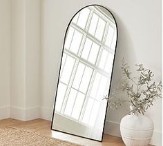 a large mirror sitting on top of a wooden floor next to a vase filled with flowers