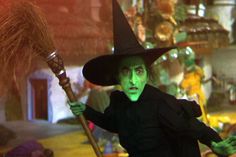 a woman dressed as the wizard holding a broom and wearing green paint on her face