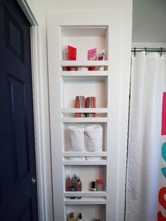 a bathroom with white shelves filled with toilet paper and other items on the shelf in front of the door