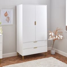 a white armoire with two drawers and a vase on the floor next to it