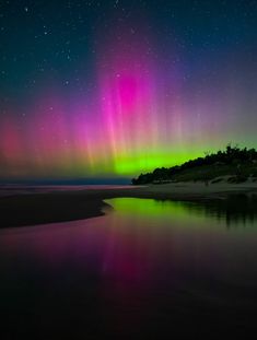 an aurora bore is reflected in the water on a beach with sand and trees under it