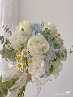 a bouquet of white and blue flowers with greenery on the stems in front of a window