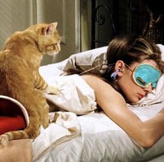 a woman laying in bed with a sleeping mask on her face next to a cat