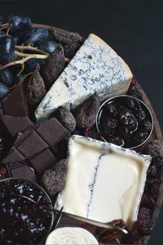 a platter filled with different types of cheeses and crackers next to grapes