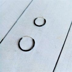 Black Hoop Earrings made by Silver Sterling 925. You can choose Size: - 10mm diameter x 1,2mm - 12mm diameter x 1,2mm - 14mm diameter x 1,2mm The black color is achieved by enameling silver with Ruthenium. In the seafaring tradition, the number of rings a sailor wore indicated the voyages he had completed. 1 hoop Cape Horn, 2 Cape of Good Hope, 3 Hoops around the world. Our earrings are sent in wooden boxes silk-screened by us, the boxes are made of recycled wood from the North of Galicia (Spain Black Minimalist Sterling Silver Cartilage Earrings, Black Single Huggie Earring As A Gift, Minimalist Black Small Hoop Huggie Earrings, Minimalist Black Round Cartilage Earrings, Everyday Black Single Hoop Earring, Black Sterling Silver Hoop Earrings For Everyday, Black Round Cartilage Earrings For Everyday Wear, Black Small Hoop Cartilage Earrings For Everyday, Minimalist Black Hoop Cartilage Earrings