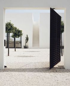 an open door leading to a white building with stairs and trees in the background,