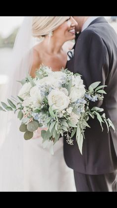 a bride and groom kissing in front of the camera with their wedding bouquet on her shoulder