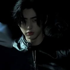 a young man with black hair wearing a leather jacket and looking at something in the distance