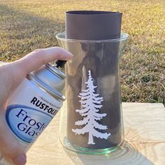 a person holding a spray bottle next to a glass with a pine tree painted on it