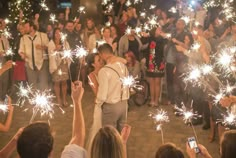 a couple kissing while surrounded by people holding sparklers