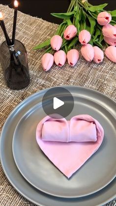 a heart shaped napkin on top of a plate next to candles and pink tulips