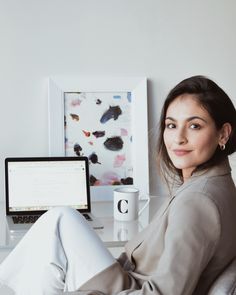 a woman sitting in front of a laptop computer on top of a white desk next to a cup