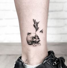 a small tattoo on the ankle of a woman with a skull and an arrow in it