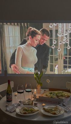 a table with food and wine on it in front of a tv screen showing a man and woman