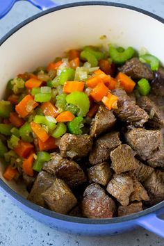 a pot filled with meat and vegetables on top of a counter next to a blue spatula