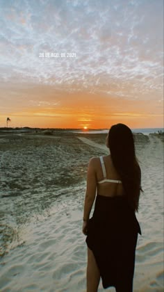 a woman standing on top of a beach next to the ocean under a cloudy sky