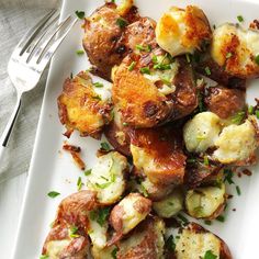 a white plate topped with potatoes covered in sauce and parsley next to a fork