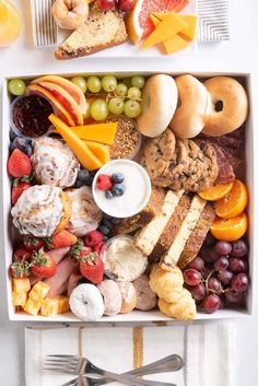 a box filled with lots of different types of food next to silverware and forks