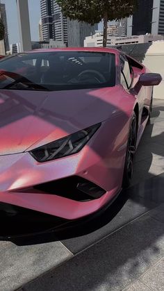 a pink sports car parked in front of a tall building with skyscrapers behind it