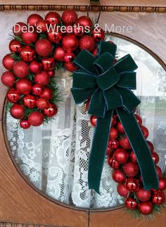 a christmas wreath with red balls and green ribbon on a wooden door frame that has lace doily around it