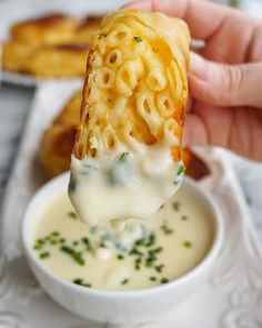 a hand holding a piece of food over a bowl of soup and dipping sauce on the side