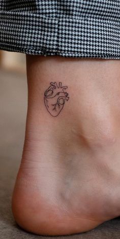 a small heart tattoo on the side of a woman's foot, which is black and white