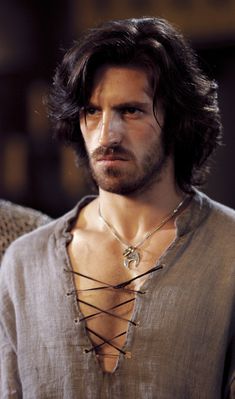 a man with long hair and a beard wearing a chain around his neck is looking at the camera