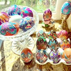 an assortment of colorful painted eggs on a counter next to a glass bowl and vase