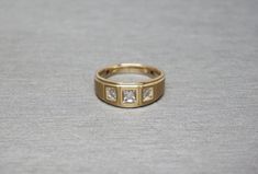 a yellow gold ring with three diamonds on the outside and in the middle, sitting on a gray surface