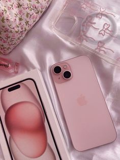 two pink iphones sitting on top of a bed next to a clear box with an object in it