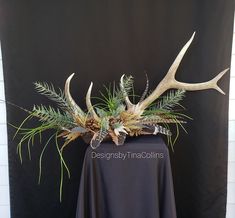 an arrangement of plants and antlers in a vase on a black cloth tablecloth