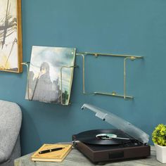 a record player sitting on top of a wooden table next to a gray chair and potted plant