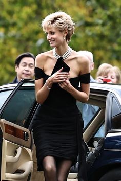 a woman in a black dress standing next to a car