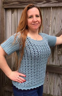 a woman standing in front of a wooden fence wearing a blue crochet top