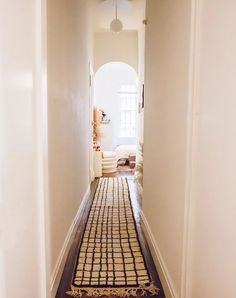 a hallway with a rug on the floor next to a lamp and door way leading into a living room