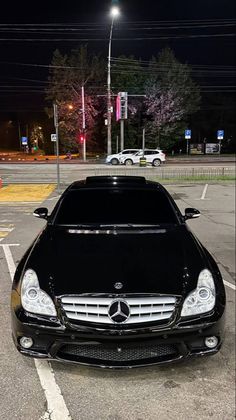 a black mercedes benz parked in a parking lot at night with the headlights turned on