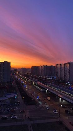 the sun is setting over a city with tall buildings and cars on the street below