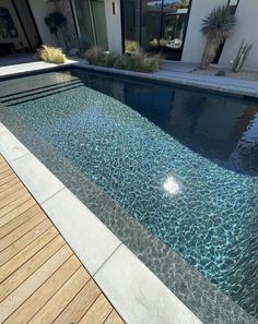 an empty swimming pool in front of a house with wooden decking and glass doors