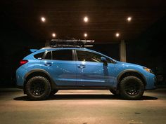 a blue subarunt is parked in a parking lot at night with its lights on