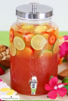 a jar filled with fruit and lemonade on top of a table next to flowers