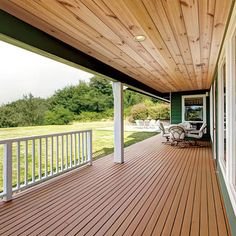 a wooden porch with white railings and chairs on the front deck overlooking an open field