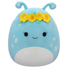 a blue stuffed animal with yellow flowers on it's head and eyes, sitting in front of a white background