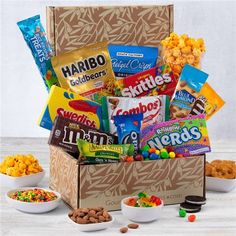 a box filled with candy and snacks on top of a wooden table next to bowls