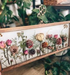 a wooden frame with dried flowers on it and greenery in the backround