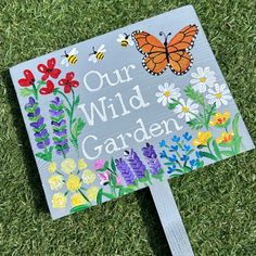 a sign that says, our wild garden on the grass with flowers and butterflies painted on it