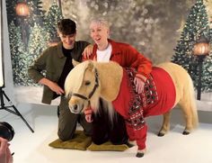 two people posing with a fake horse in front of a christmas tree backdrop and lights