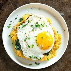 an egg is sitting on top of some food in a white plate with green garnish