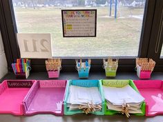 colorful trays with writing on them are sitting in front of a window, next to a bulletin board