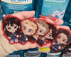 someone is holding three keychains with anime characters on them in front of bottles of mouthwash