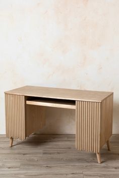 a wooden desk sitting on top of a hard wood floor next to a white wall